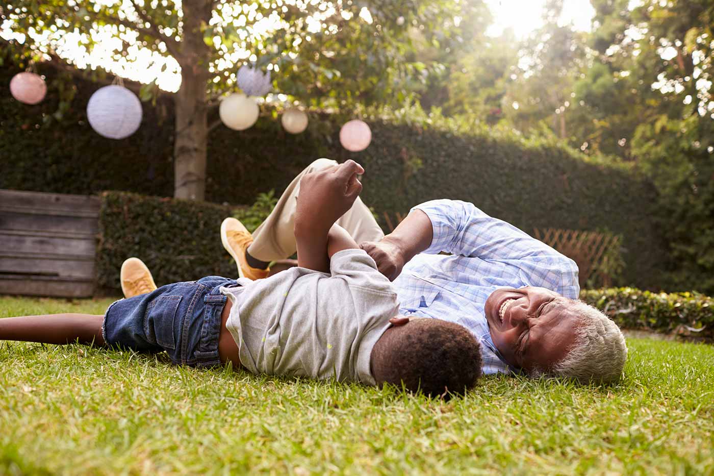 Grandfather and grandson lying on ground enjoying landscaped yard.