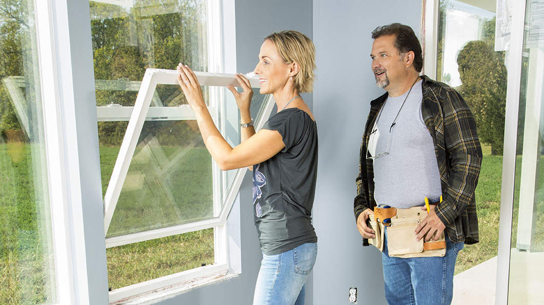 Woman opening new double hung windows as  home contractor watches.