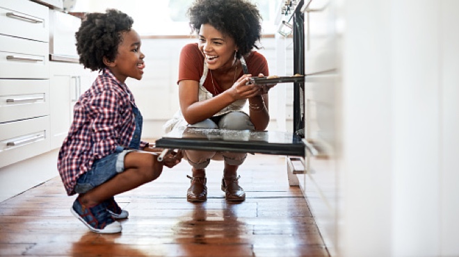 Mother and child placing pan of cookies into oven.