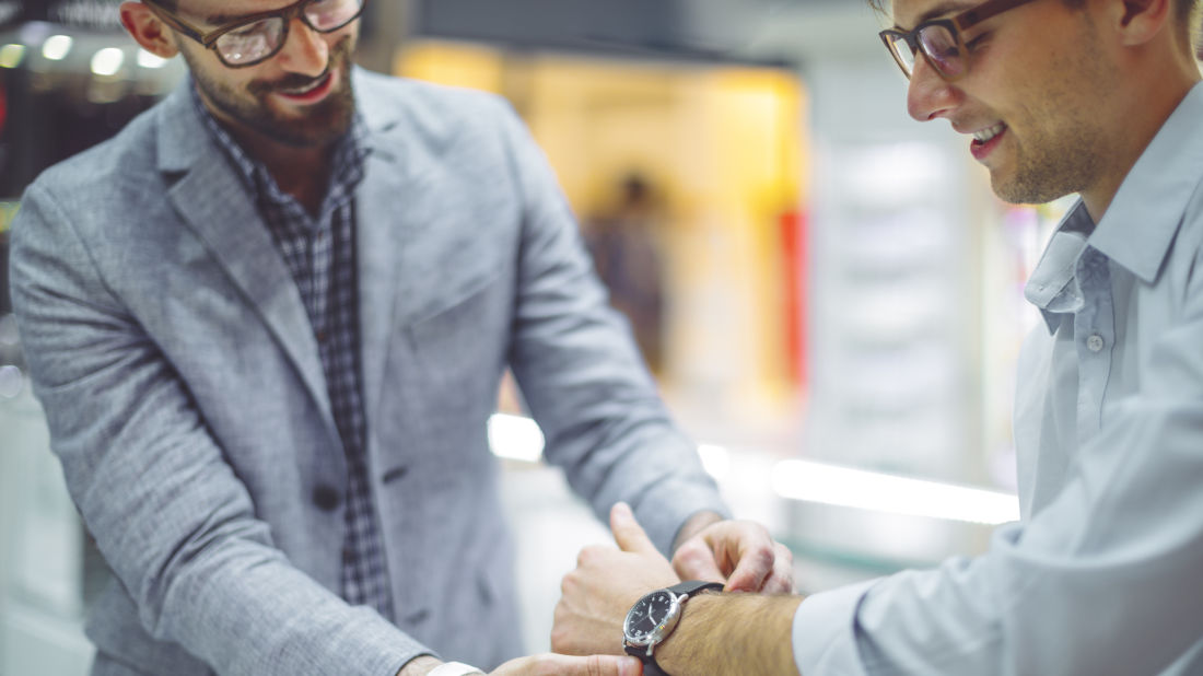 Store associate helping shopper try on wrist watch.